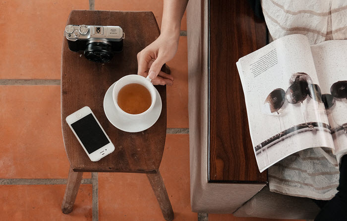 woman reading magazine with phone and coffee on table beside her