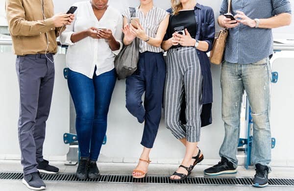 diverse group of people leaning against a wall and using smartphones