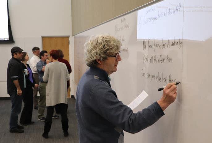 Michael Murray writes on a white board as other professors talk in the background